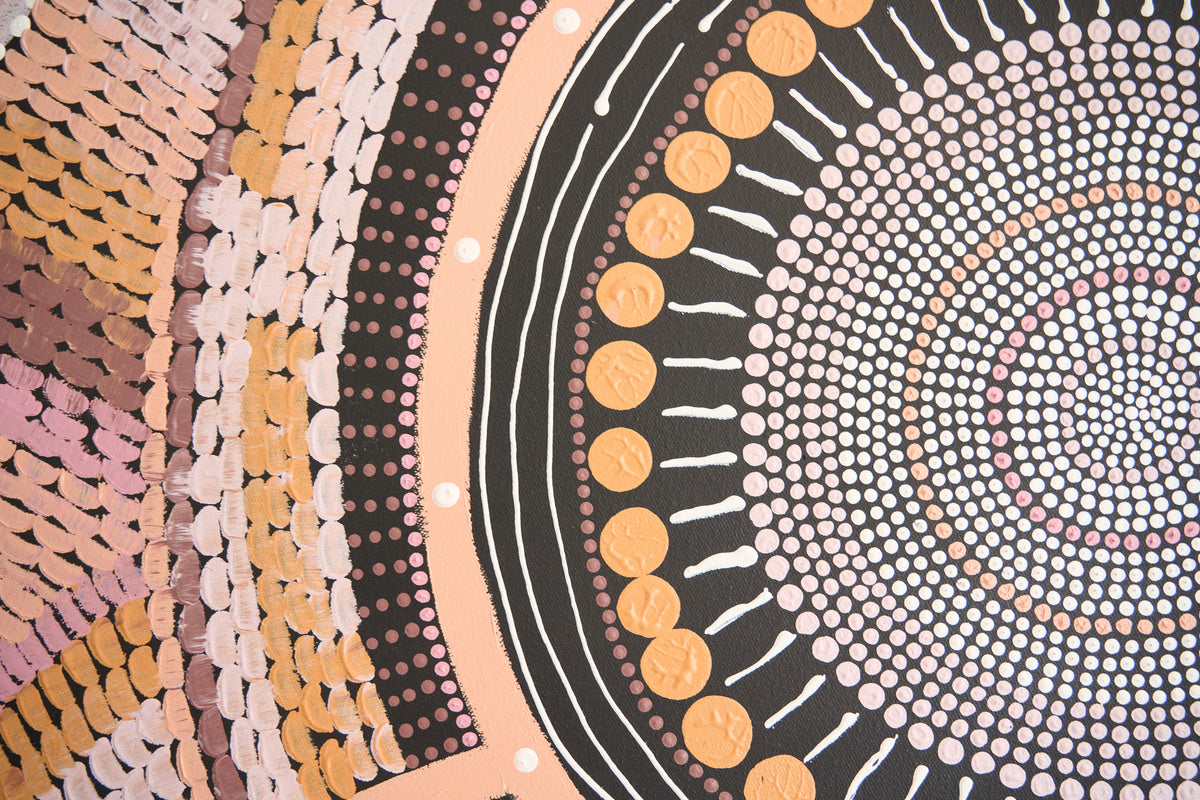 A close-up of a circular Aboriginal-style dot painting with concentric circles, white lines, black bands, peach and pink bands, and rows of gold and orange dots.