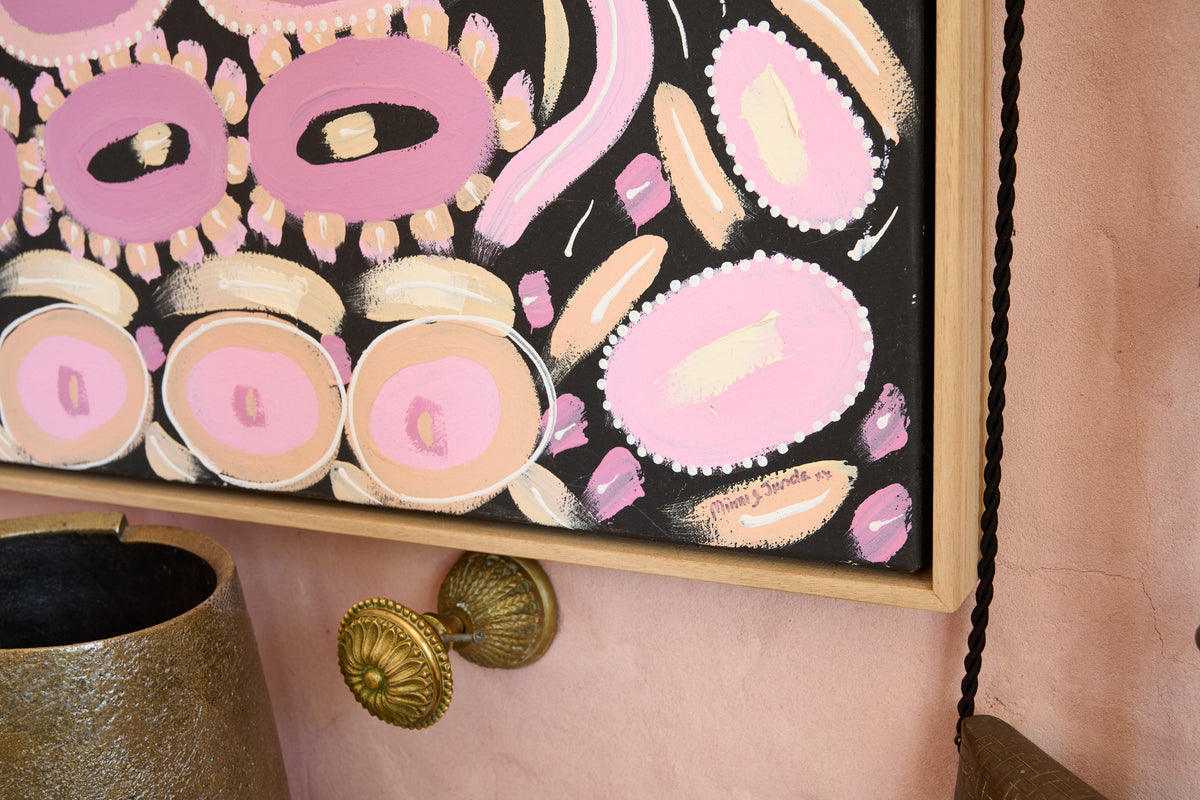 Abstract framed wall art featuring pink, cream, and peach organic shapes on a black background, mounted on a blush pink wall above brass hardware.