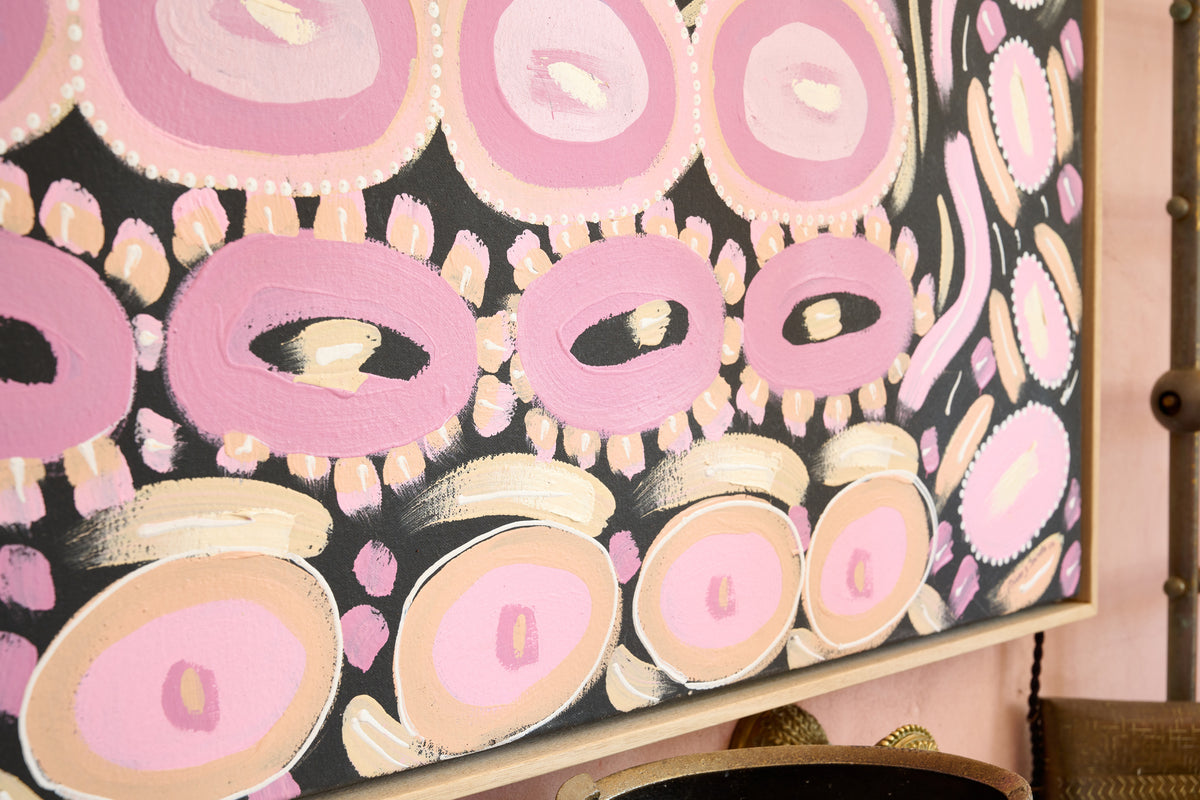 Abstract framed wall art featuring pink and cream circular motifs on a black background, shown hanging in a pink room.