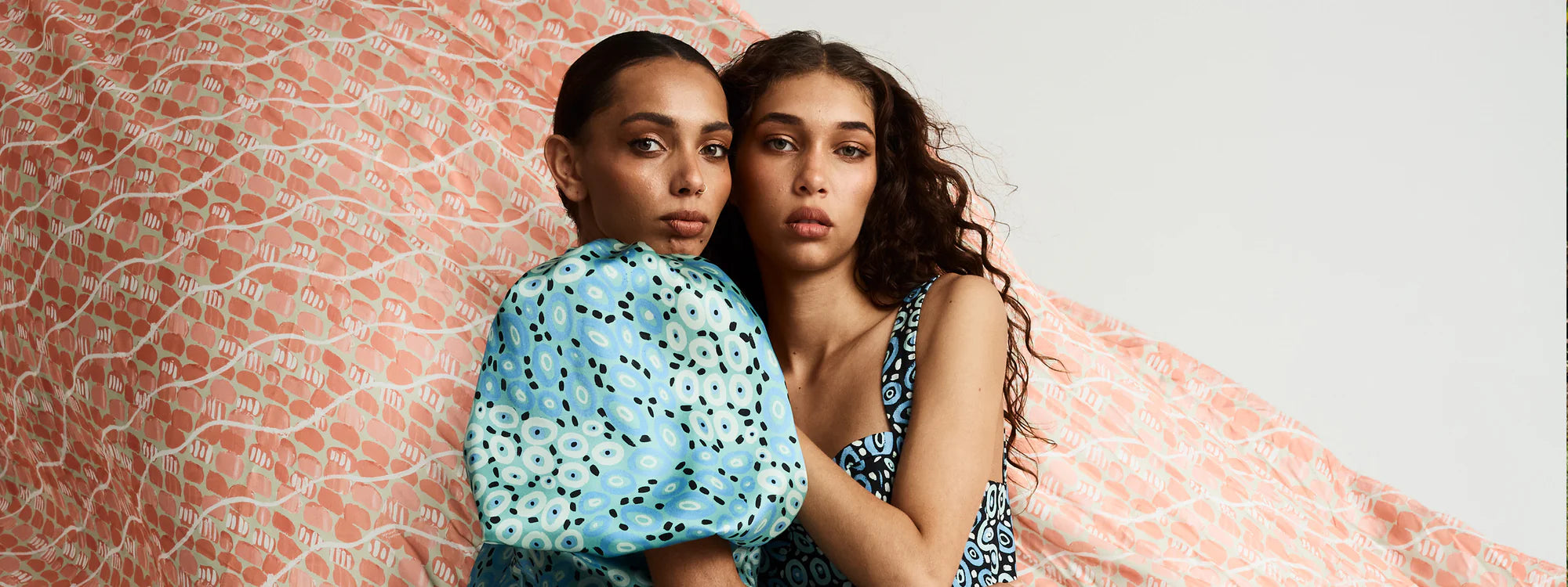 Two women standing close together against a textured pink and white background