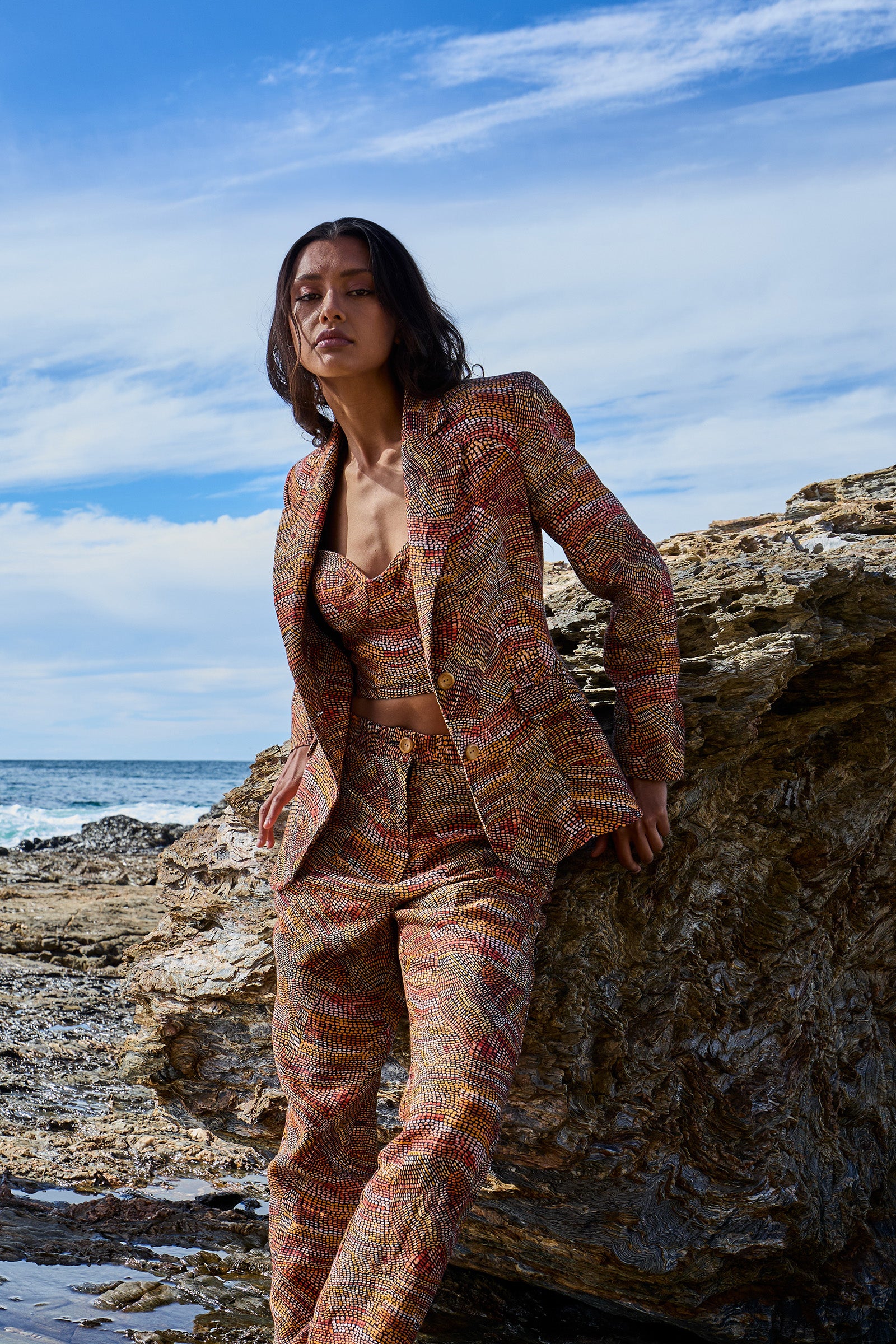 A woman standing on a rocky beach wearing a floral print linen slimline comfort jacket and matching pants.
