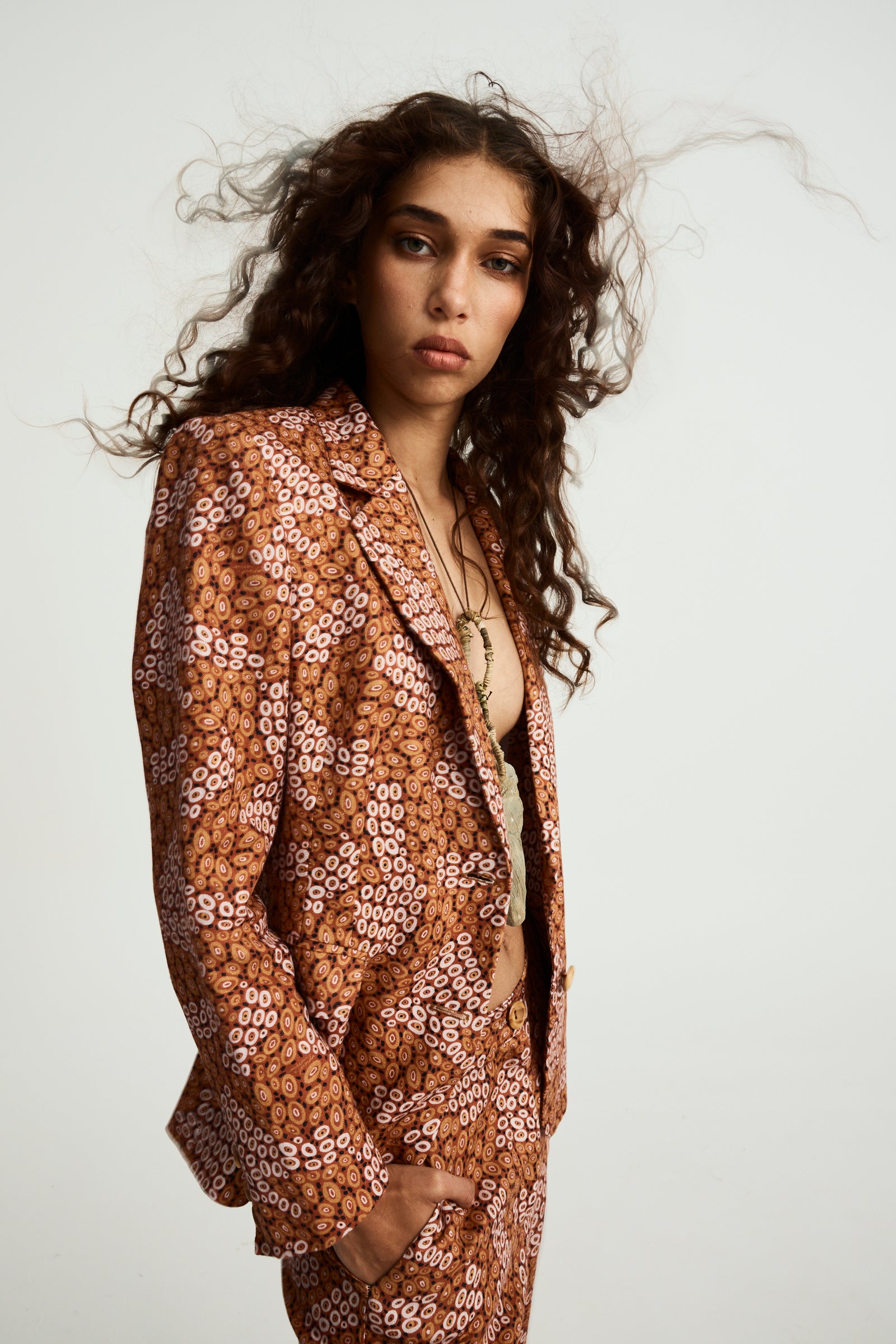 A model wearing an ochre linen slimline comfort jacket with an abstract pattern. The jacket has wooden buttons and is tailored with darts at the back and sides.