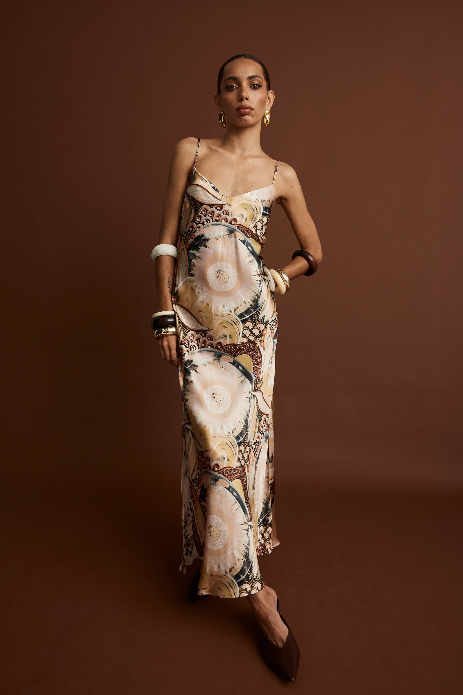 A model wearing a floral and geometric patterned silk slip dress with side slits and thin straps.