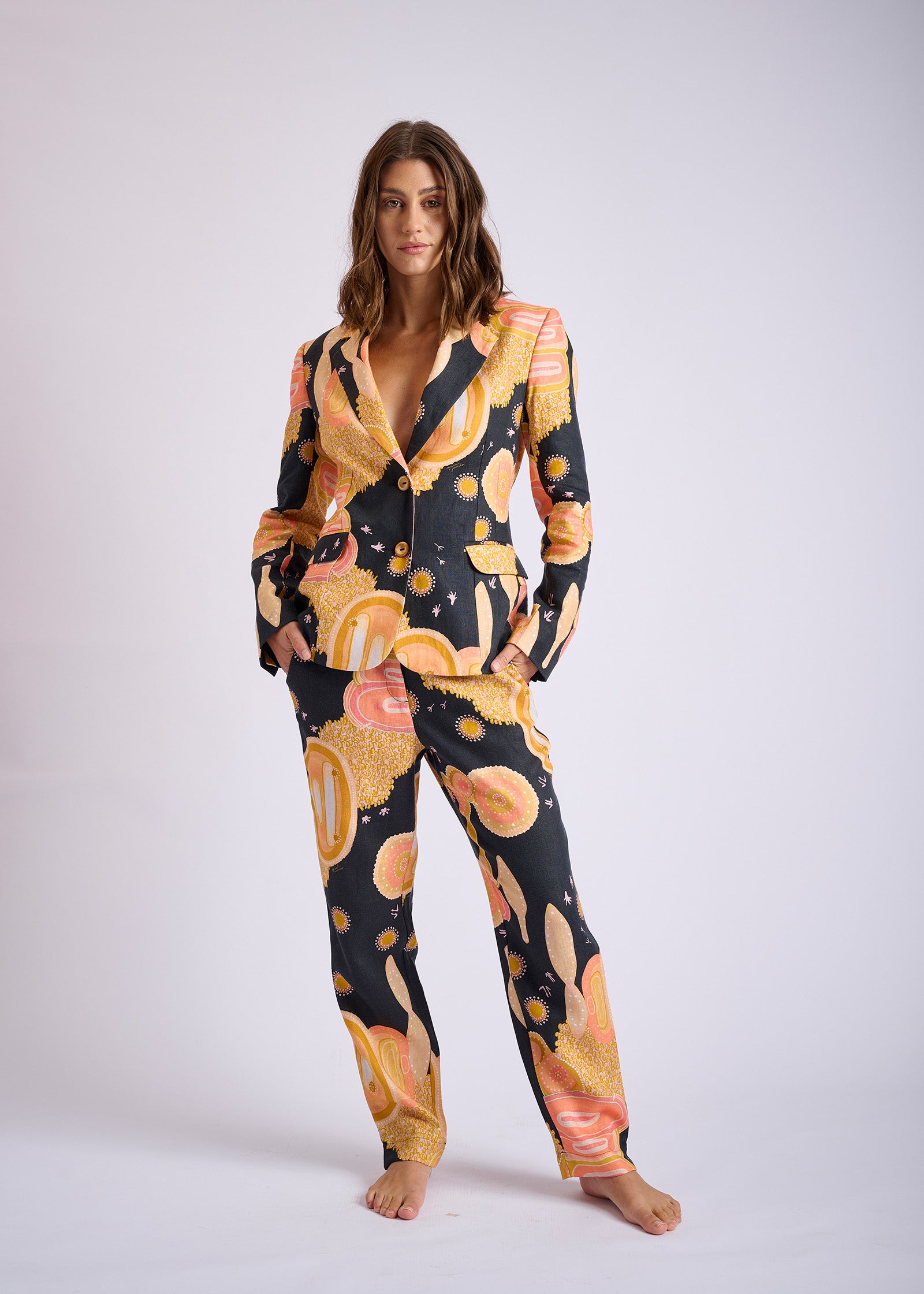 A model wearing a relaxed fit linen pants with a tapered leg and side pockets, featuring a multicolored abstract print.