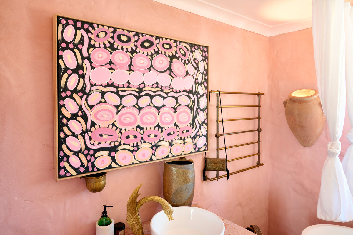 A large framed abstract art print featuring pink, black, and white organic shapes, displayed on a pink plaster bathroom wall above a white sink with a gold faucet.