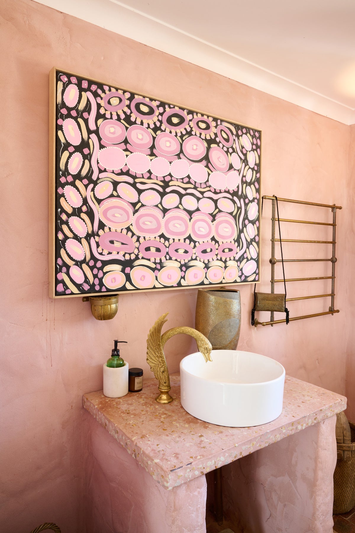 A pink and black abstract patterned wall art print with gold accents, displayed in a bathroom setting above a pink stone vanity with a white vessel sink and gold faucet.