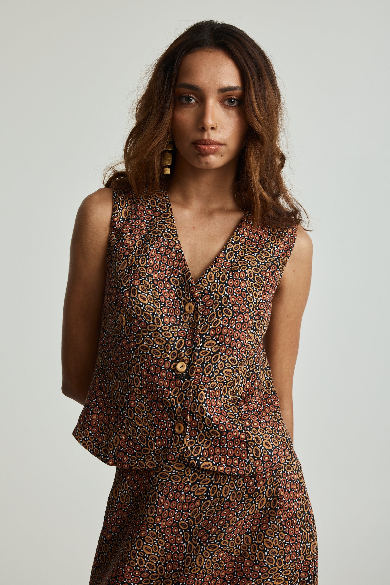 A woman wearing a sleeveless, button-up Jibaanga Chocolate Linen Vest with a v-neckline, showcasing a multicolored animal print.