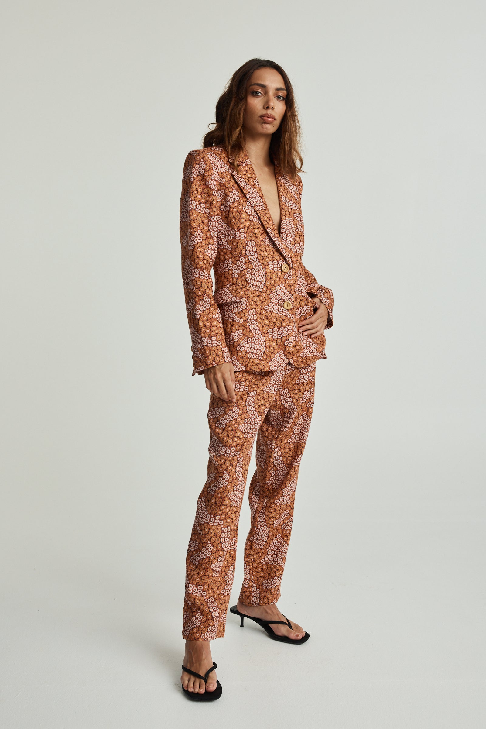 A model wearing an ochre linen pantsuit with an aboriginal print, featuring a relaxed fit with functional side pockets and a tapered leg.