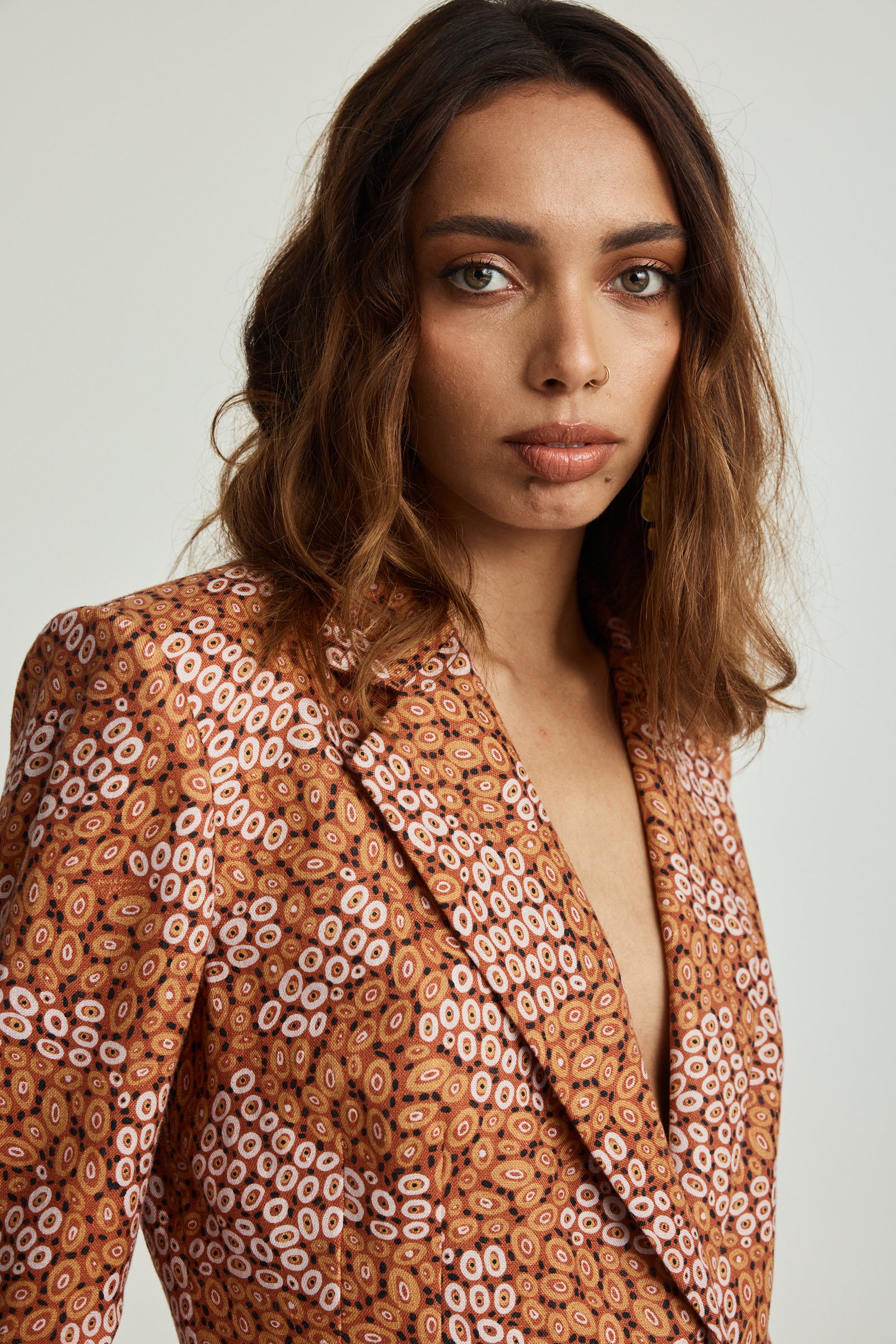 A model wearing an ochre linen slimline comfort jacket with a geometric print, featuring front pockets and wooden buttons.