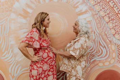 Two women standing close together against a decorative wall with circular patterns.