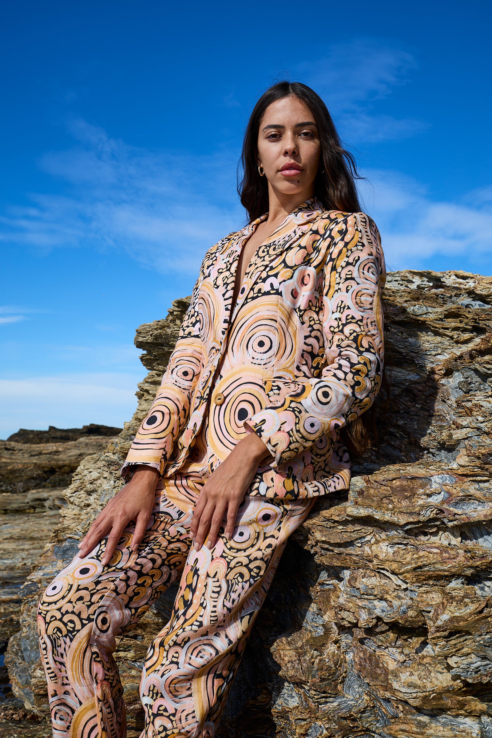 Woman in a patterned outfit sitting on rocks with a blue sky background